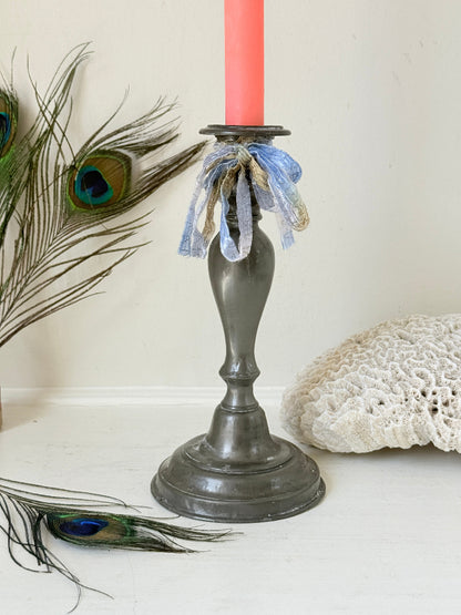 Antique pewter candlestick with baluster stem and aged patina styled with coral candle on white surface