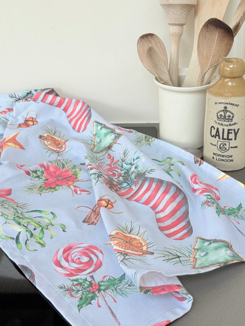 Blue Loft Christmas cotton tea towel with red striped stocking and festive motif pattern photographed on a white worktop.