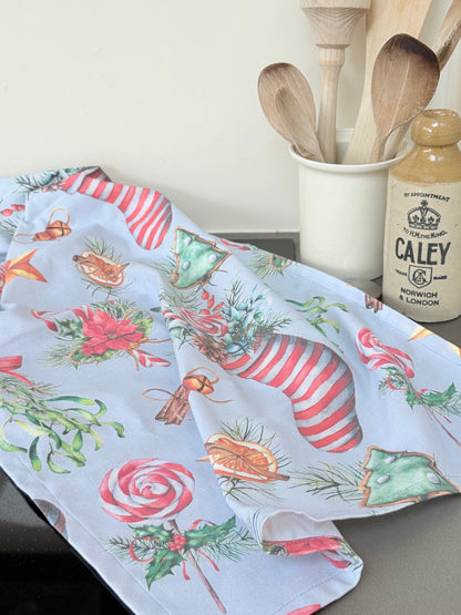 Blue Loft Christmas cotton tea towel with red striped stocking and festive motif pattern photographed on a white worktop.