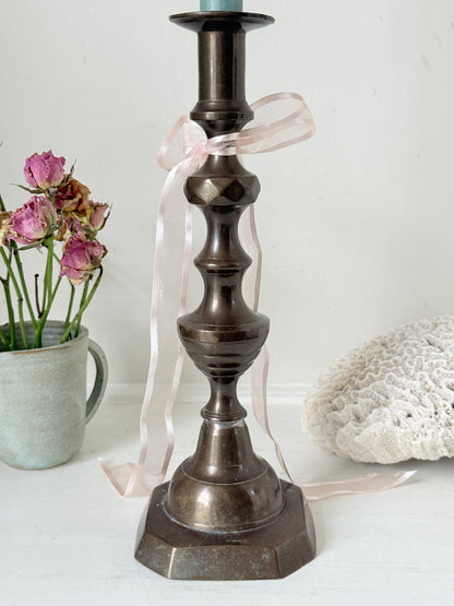 Bronze coloured vintage candlestick with bobbin stem and shaped base styled with taper candle on white surface