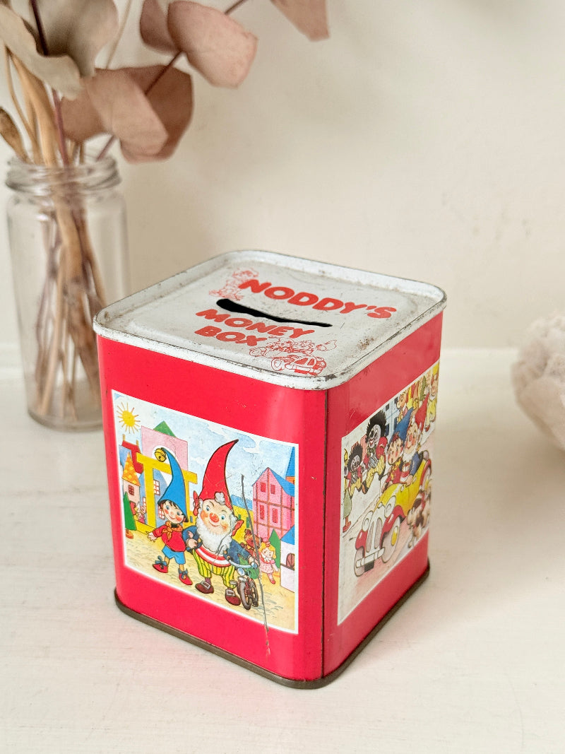 Vintage Noddy money box tin in red with illustrated panels, photographed on a white surface