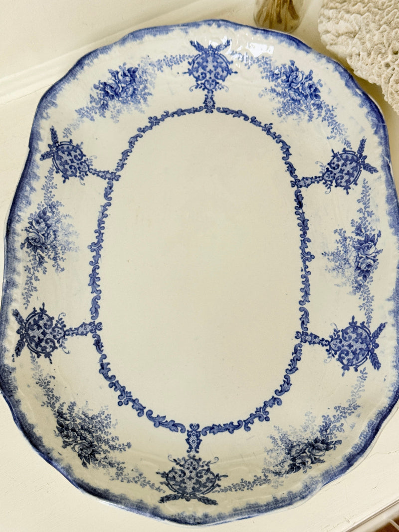 Antique oval blue and white platter with floral border photographed on a white surface