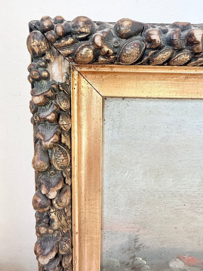Close-up of an ornate vintage picture frame corner, featuring a textured shell-like carved border in dark brown and gold tones, with a gold inner frame and a light gray mirror or glass surface.