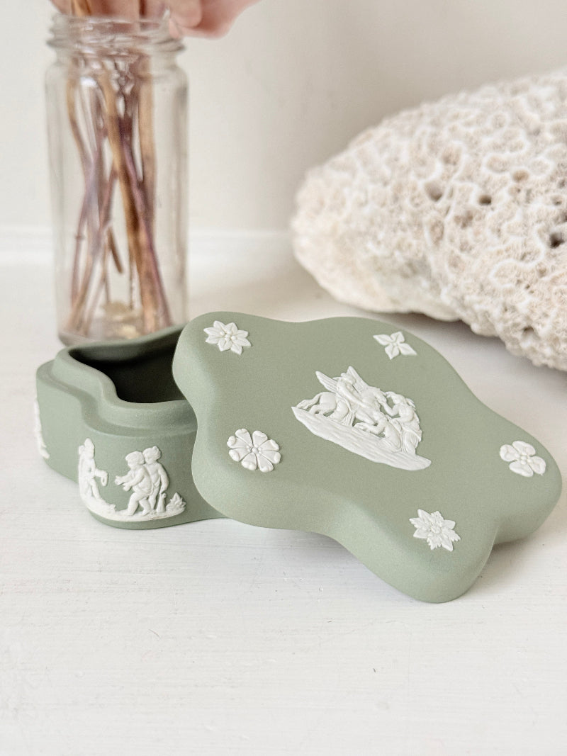 Vintage Wedgwood Jasperware sage green lidded trinket box in a quatrefoil shape, decorated with white neoclassical cherubs and florets, styled with dried stems.