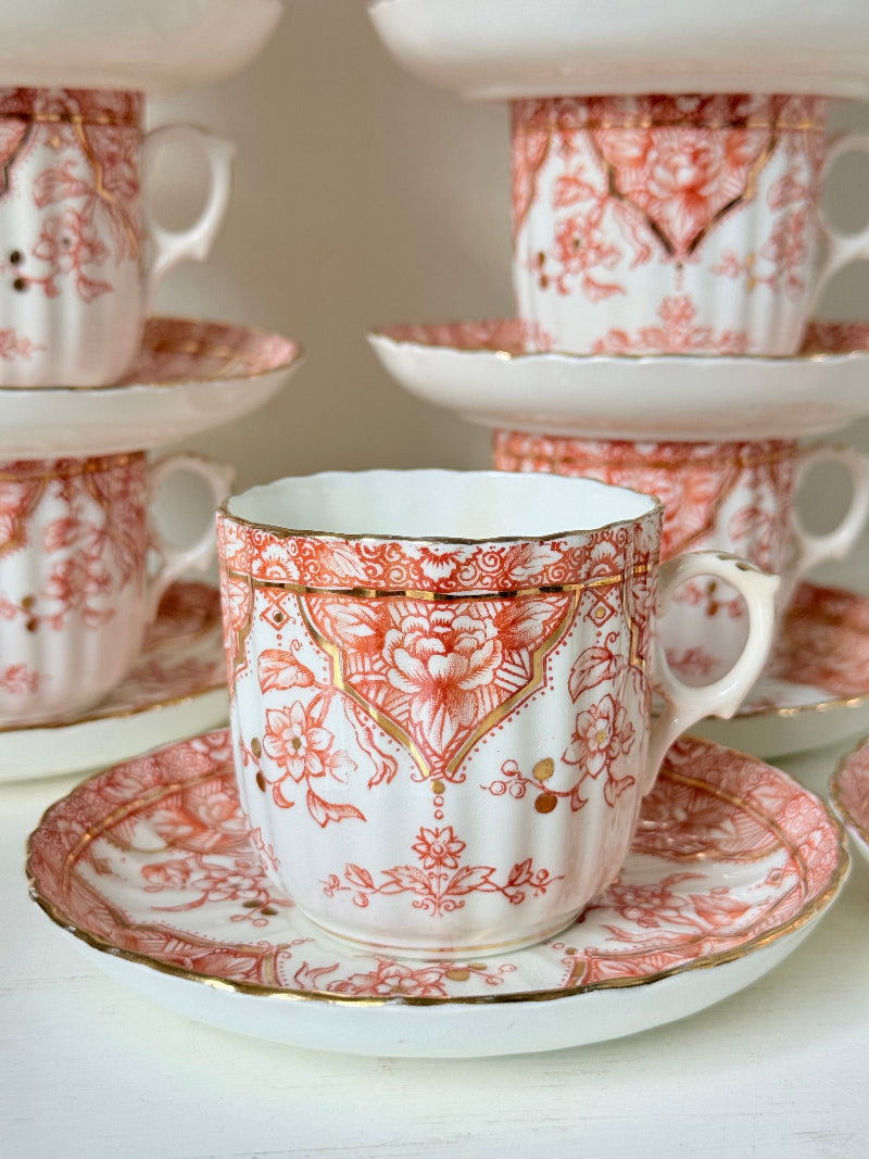 Vintage coral transferware coffee cans and saucers with scalloped edges and gold accents, set of ten, styled on a white surface.