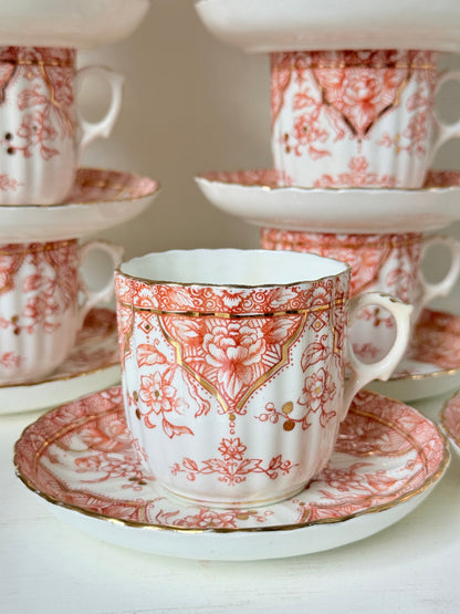 Vintage coral transferware coffee cans and saucers with scalloped edges and gold accents, set of ten, styled on a white surface.