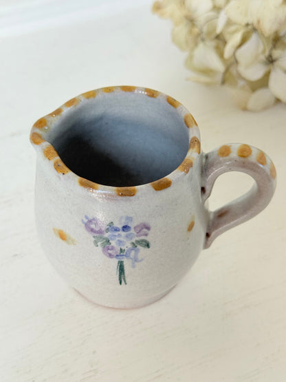 vintage studio pottery milk jug with hand painted lilac flowers and ochre rim photographed on white surface
