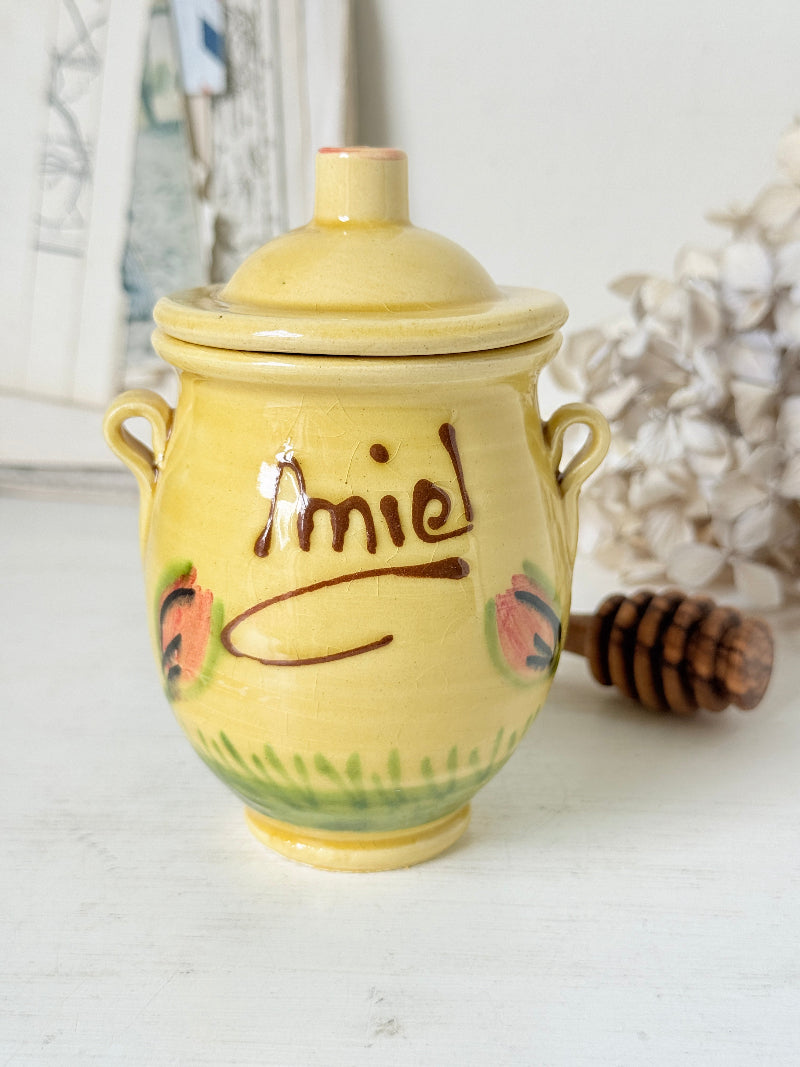 A yellow ceramic honey pot with a lid, featuring the word &