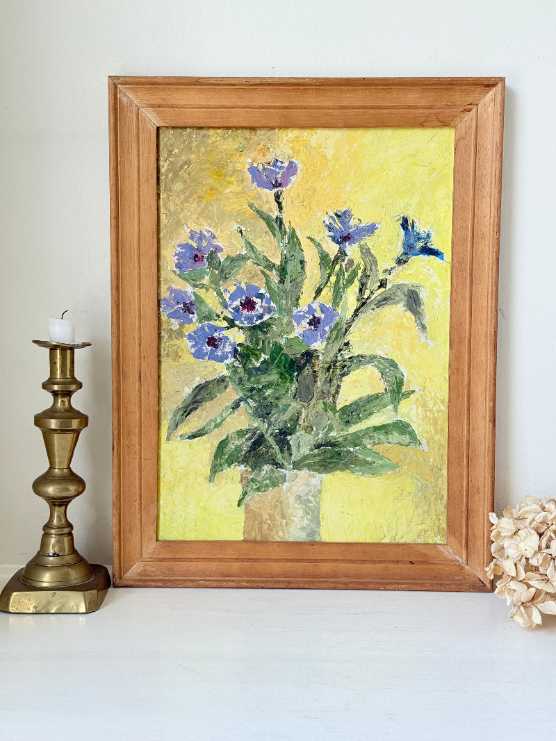 Vintage oil painting of cornflowers in a vase with yellow background in wooden frame photographed on a white surface