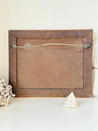 The back of a rustic wooden picture frame with a hanging wire and pinback, displayed on a white surface with decorative props.