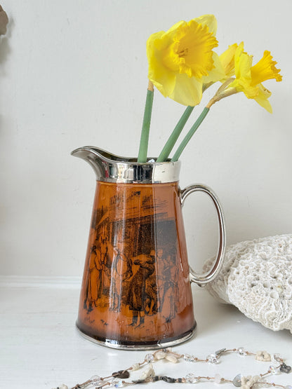Antique Ridgways stoneware jug photographed on a white surface in amber treacle glaze with black Coaching Days and Coaching Ways scenes and silver lustre rim