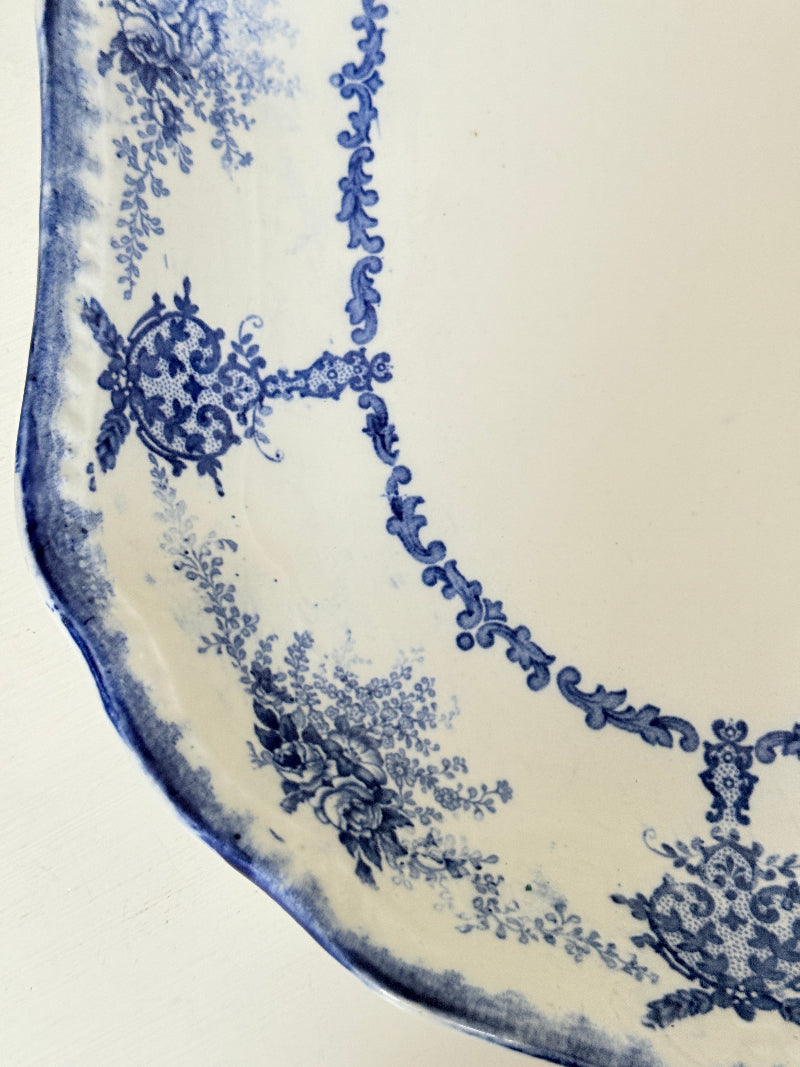 Antique oval blue and white platter with floral border photographed on a white surface