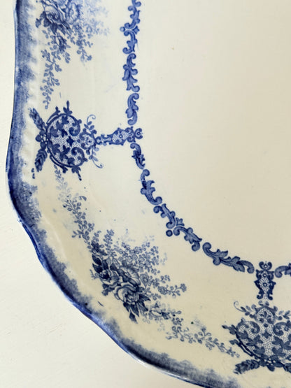 Antique oval blue and white platter with floral border photographed on a white surface