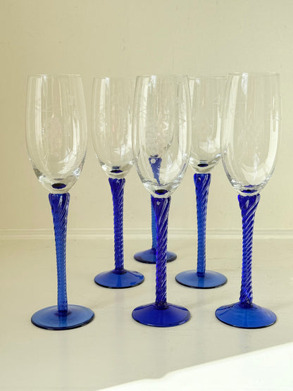 Set of six vintage French champagne flutes with tall clear bowls and cobalt blue twisted stems, photographed on white surface.