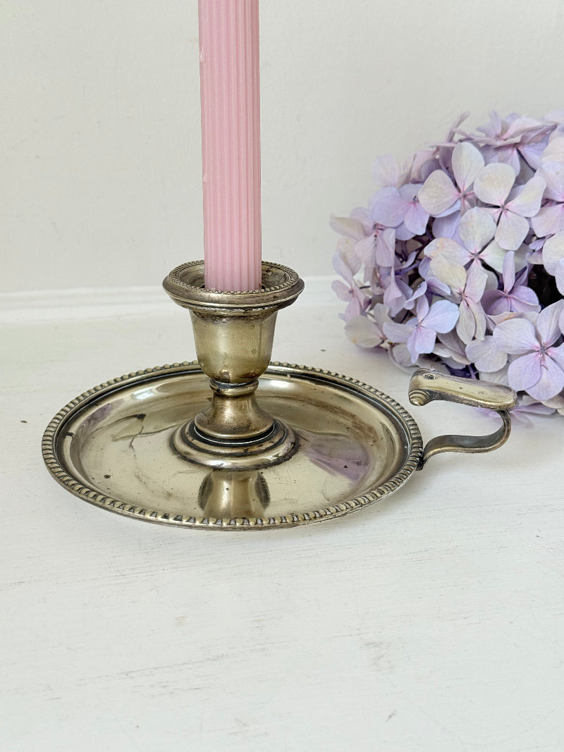 Antique silver plate chamberstick with handle, photographed on a white surface beside pink hydrangeas and vintage books
