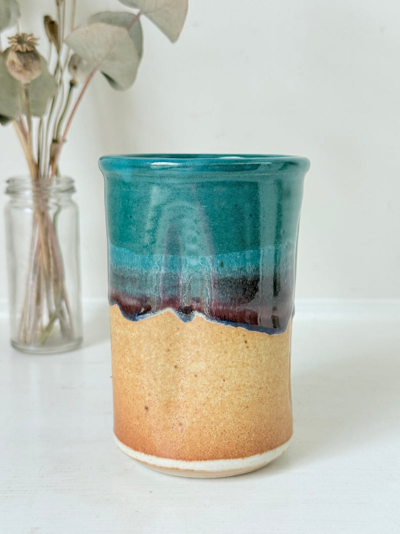 Studio pottery pen pot with teal and plum drip glaze, photographed on a white surface