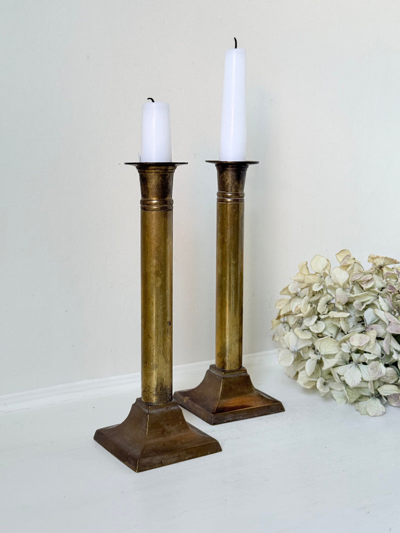 Pair of vintage brass candlesticks with square bases and white taper candles, styled on a white surface beside dried hydrangeas.