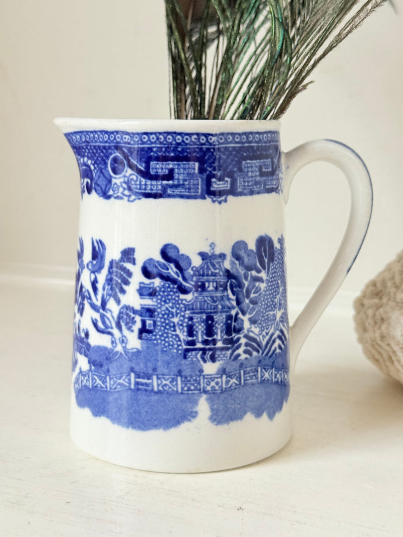 Antique Wedgwood and Co blue and white milk jug photographed on a white surface with peacock feathers.