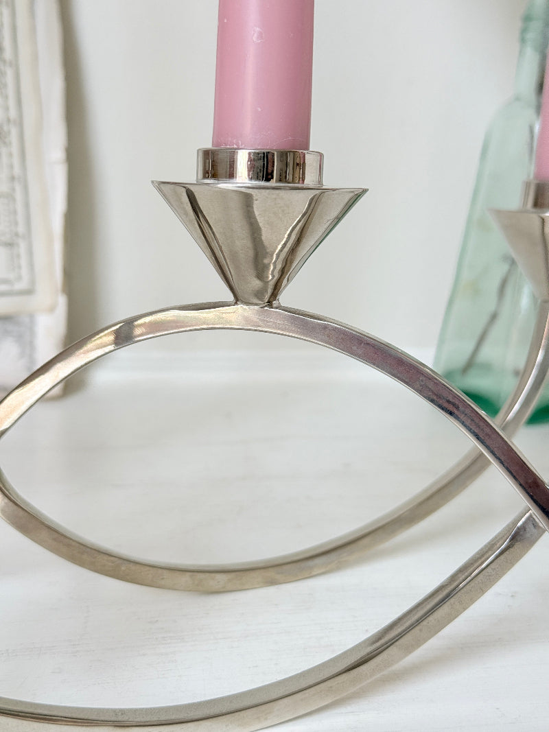 Silver tone five light candelabra with a sculptural looped base holding pink candles, photographed on a white surface