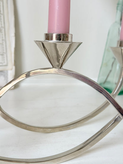 Silver tone five light candelabra with a sculptural looped base holding pink candles, photographed on a white surface