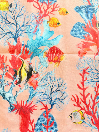 Warm peach coral and tropical fish print cotton tea towel with wooden forks on a marble surface beside cut glass