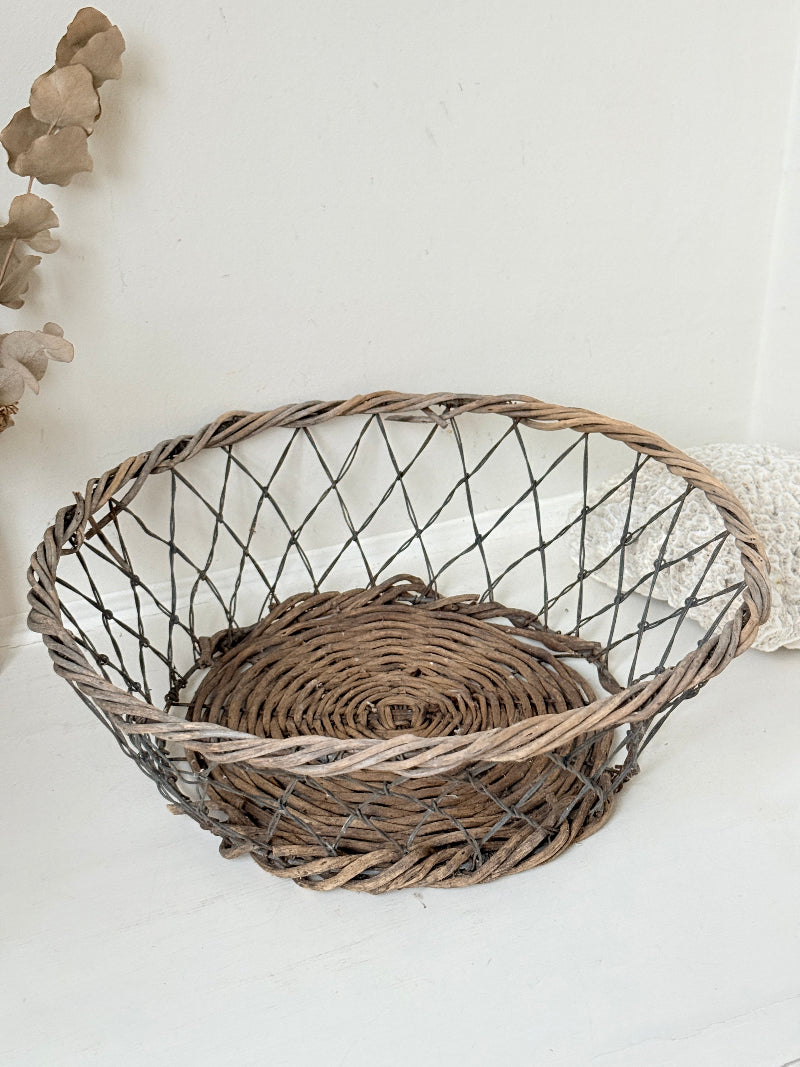 Vintage wicker and wire basket with woven base photographed on a white surface