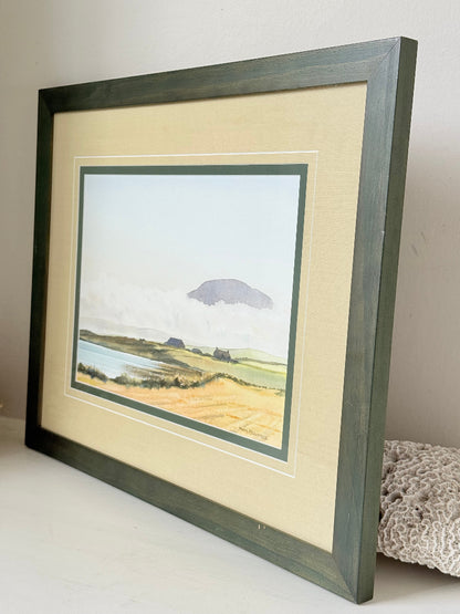 Framed Scottish watercolour coastal landscape by Martin W. M. Prentice in green frame with double mount, on white surface.