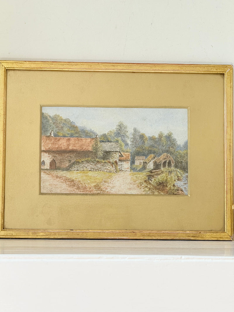 Framed vintage watercolour of countryside farm buildings with red roofs in gold frame photographed on a white surface