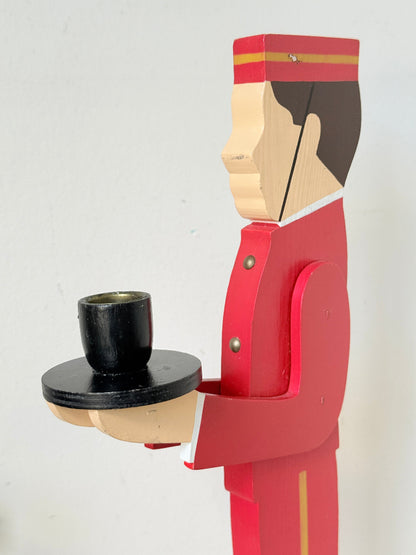 Vintage bellboy candlestick holder in red and black holding a tray with candle, photographed on a white surface