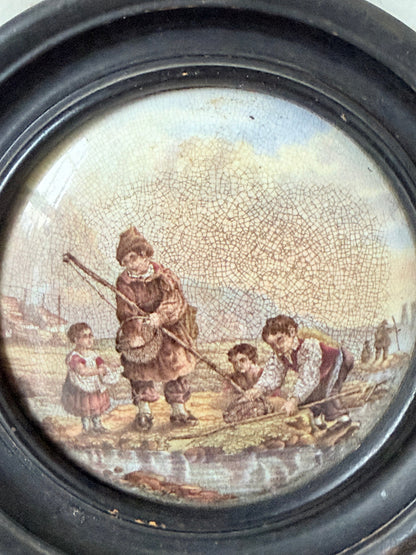 Antique Prattware framed ceramic lid with rural family scene photographed on a white surface.