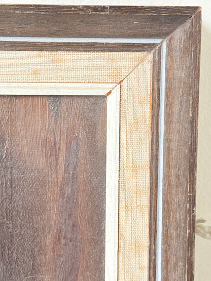 Close-up of a framed wall art corner showing layered wood trim in dark brown and medium brown tones with a light beige textured inner border and a thin white edge.