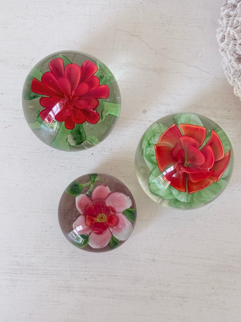 Trio of vintage glass paperweights with hand worked red floral detail, clear glass domes and green leaf decoration