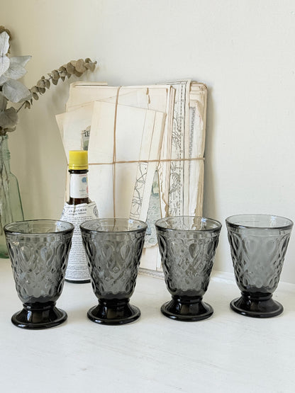 Set of four smoke grey pressed glass footed goblets with a diamond pattern, photographed on a white surface