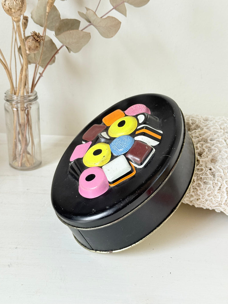 Vintage Liquorice Allsorts decorative tin with raised multicolour sweet design on black base, photographed on white surface.