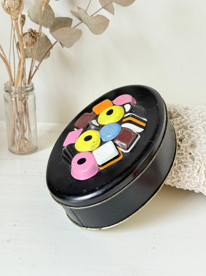 Vintage Liquorice Allsorts decorative tin with raised multicolour sweet design on black base, photographed on white surface.