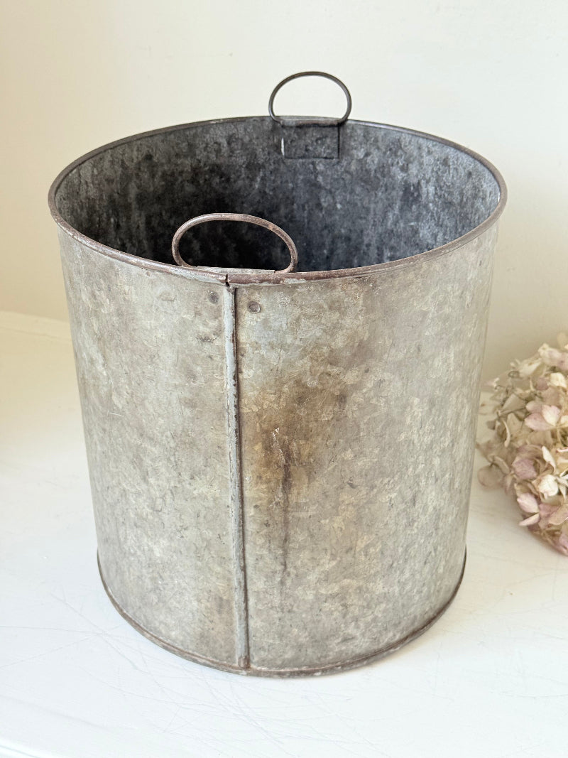 Vintage galvanised metal bin with handles, photographed on a white surface.