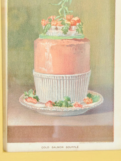 Framed Victorian cookery illustration of a celebration cake from 1896 in a mustard yellow frame displayed on a white surface.