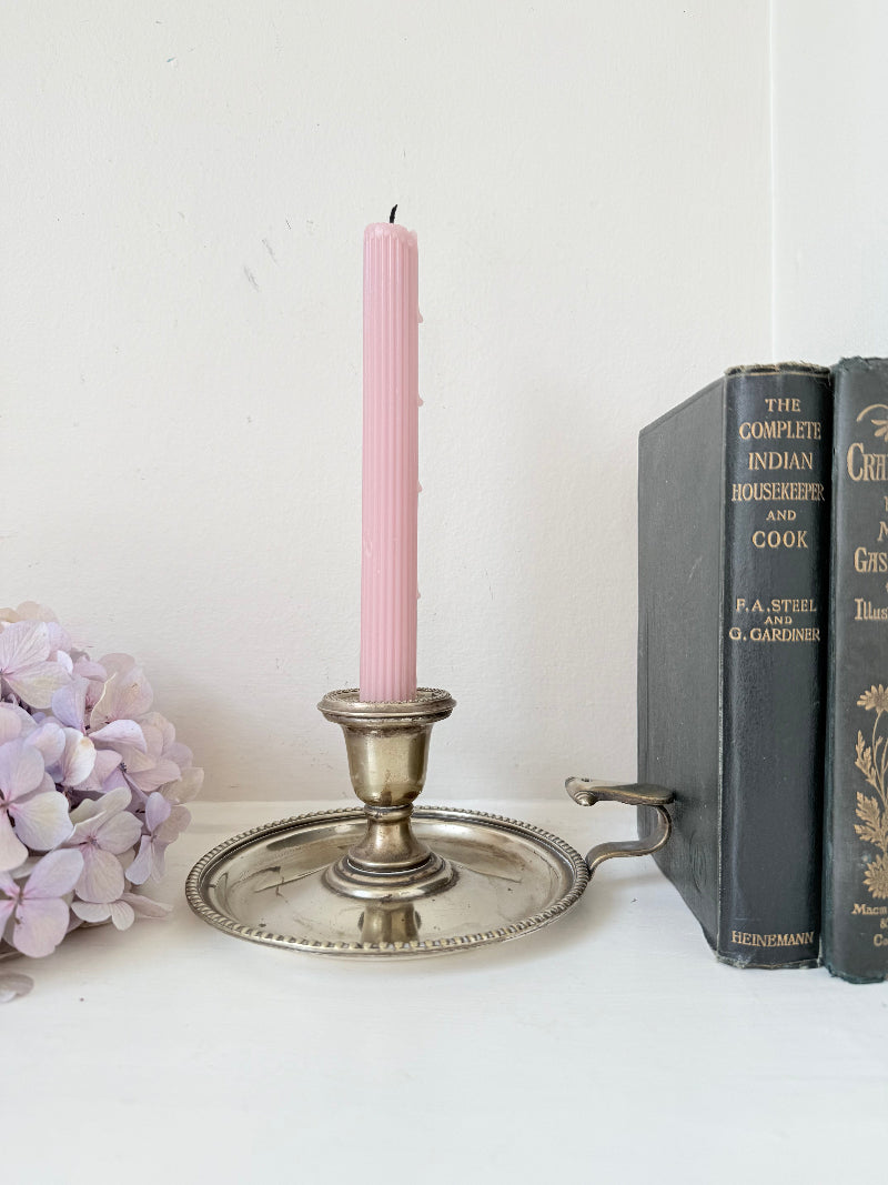 Antique silver plate chamberstick with handle, photographed on a white surface beside pink hydrangeas and vintage books