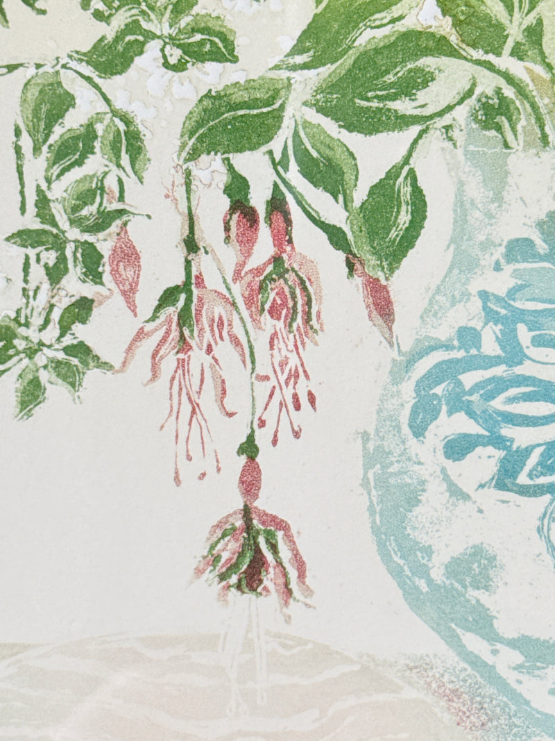 A close-up of a botanical print or textile pattern featuring green leaves and pink hanging flowers on a light cream background, with a pale blue decorative shape at the right edge.