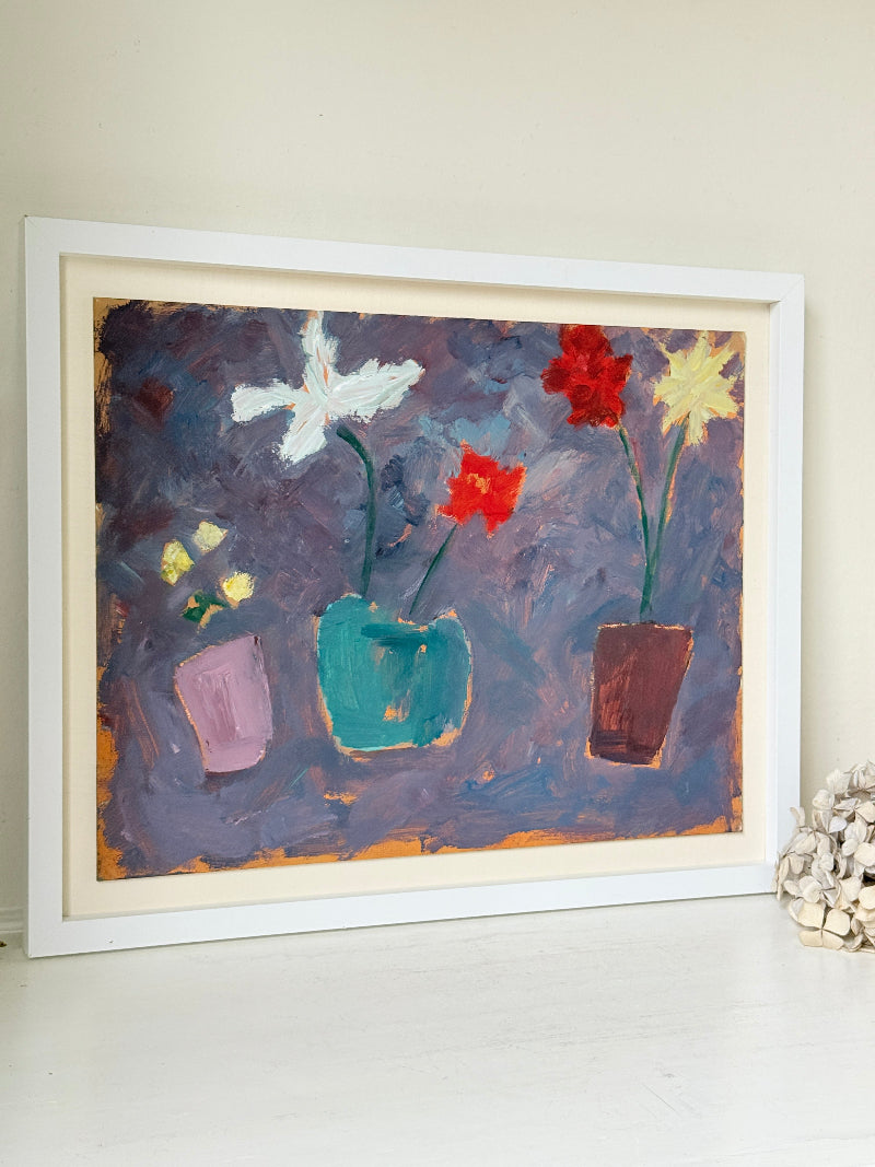 A framed painting of three colorful flower pots against a textured purple background, displayed on a white surface against a beige wall.