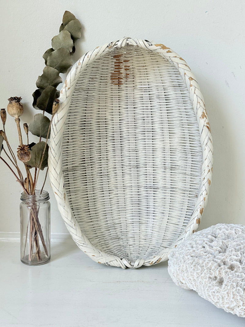 Vintage white chippy wicker basket with oval shape and worn painted finish, photographed on white surface.
