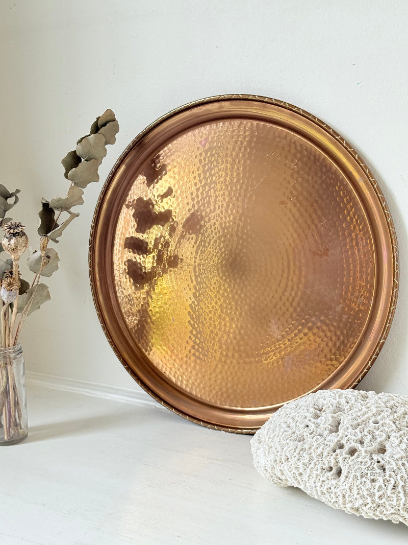 Lakeland Borrowdale hammered copper tray with warm patina, photographed on a white surface beside dried stems.