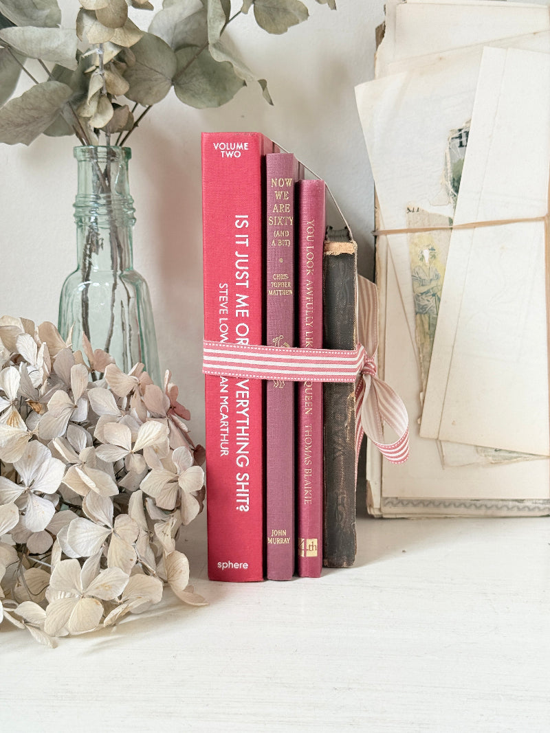 Stack of cloth bound vintage books in red and warm pink tones tied with striped ribbon and dried flowers