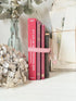 Stack of cloth bound vintage books in red and warm pink tones tied with striped ribbon and dried flowers
