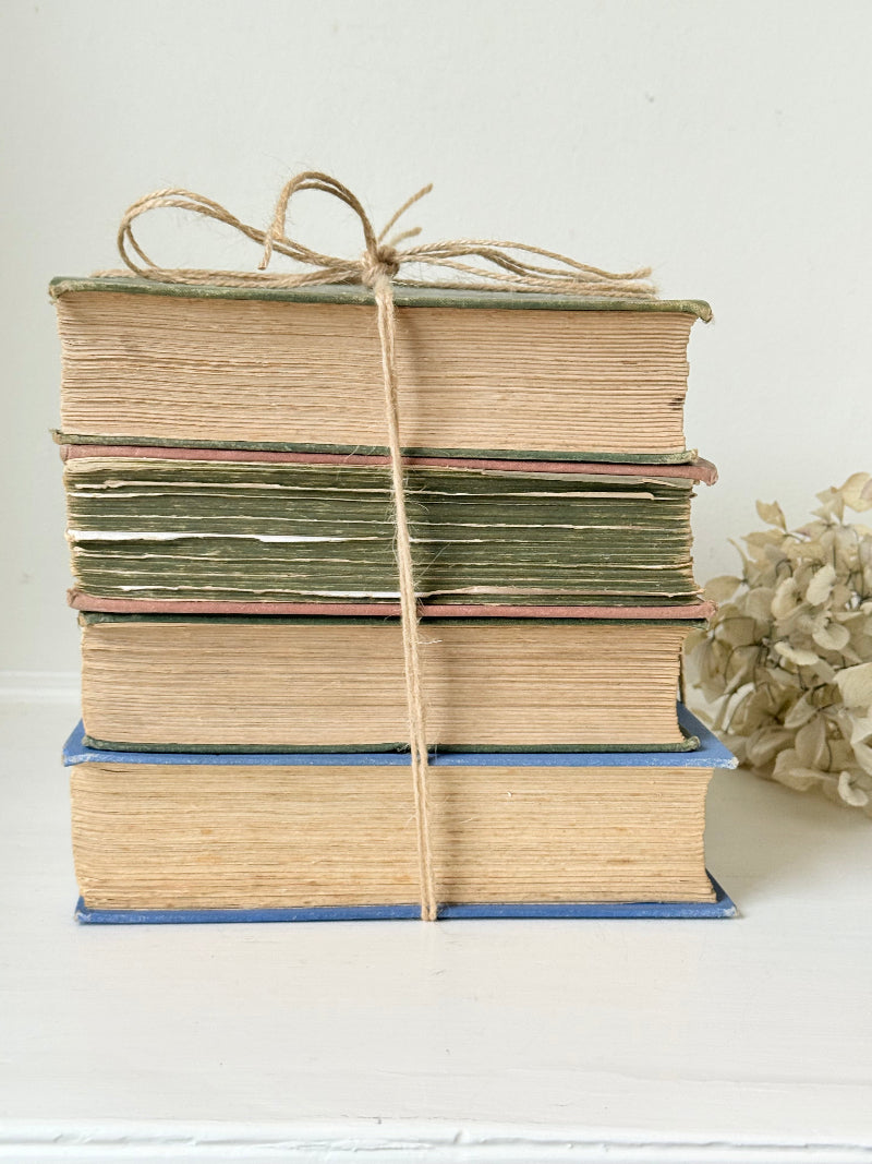 Vintage decorative book bundle in green, blue, and coral with printed lettering, tied with twine, photographed on a white surface