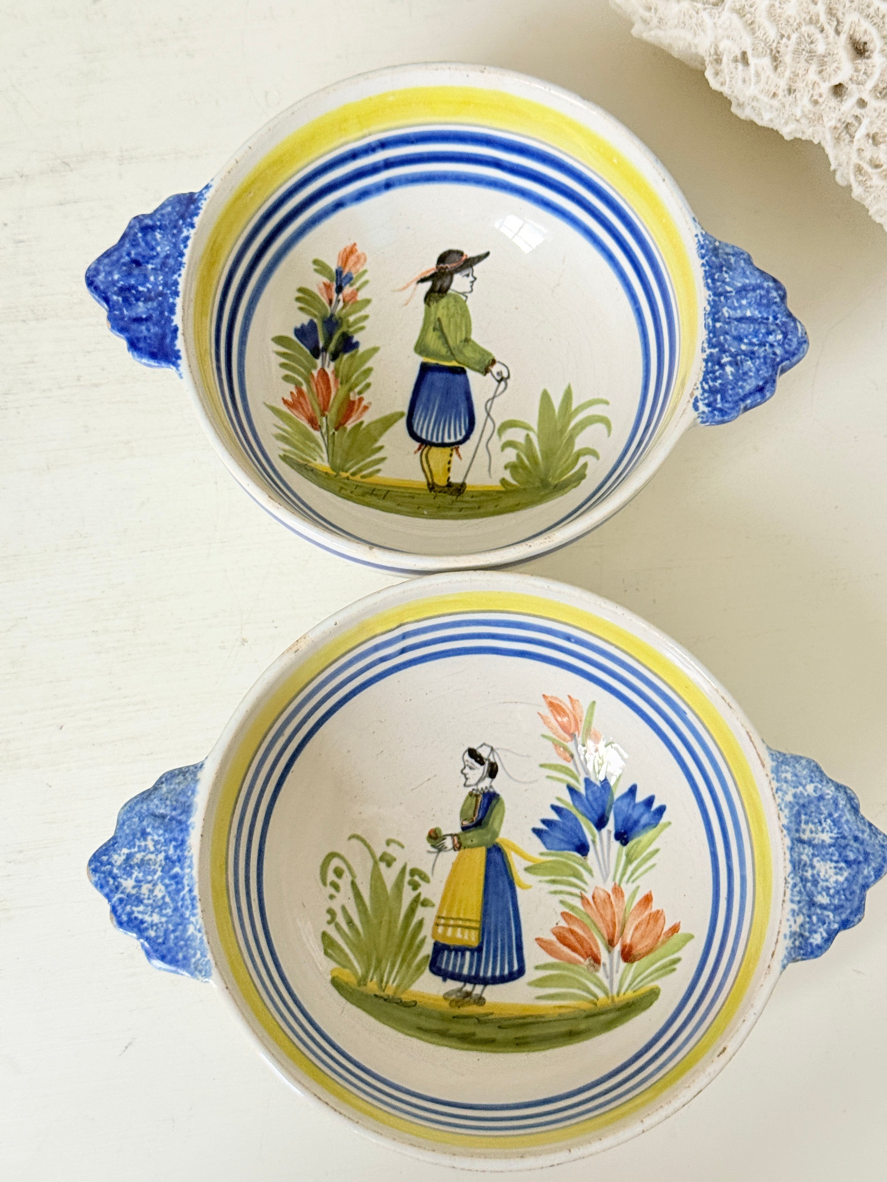 Pair of vintage French Quimper Breton figure bowls with blue handles, photographed on a white surface