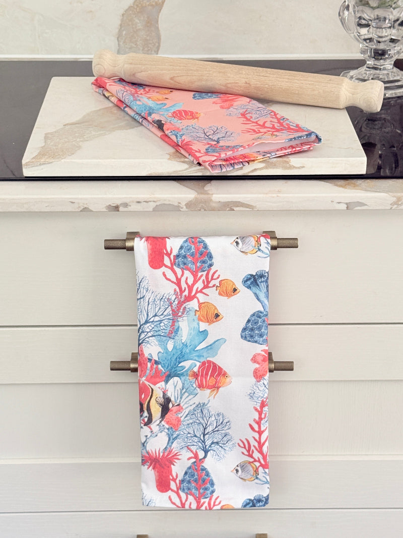 Warm peach coral and tropical fish print cotton tea towel with wooden forks on a marble surface beside cut glass
