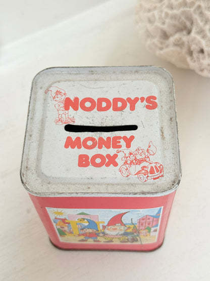 Vintage Noddy money box tin in red with illustrated panels, photographed on a white surface