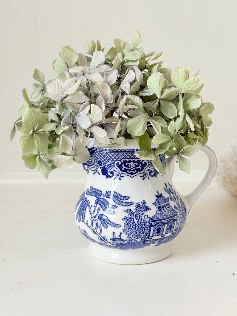 Vintage Churchill Blue Willow milk jug in blue and white ceramic photographed on a white surface.