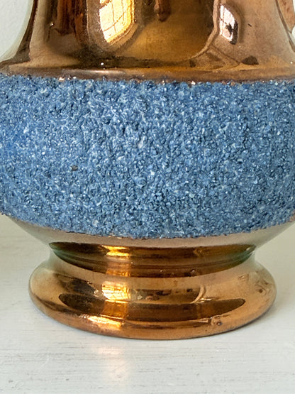 Close-up of a decorative ceramic vase or pitcher with a textured blue band around the middle and a glossy metallic copper-brown base and upper section.
